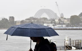 A man walks in front of the Harbour Bridge during rainfall in Sydney on 7 April as inclement weather triggered evacuation orders in several suburbs of Sydney's south and southwest.