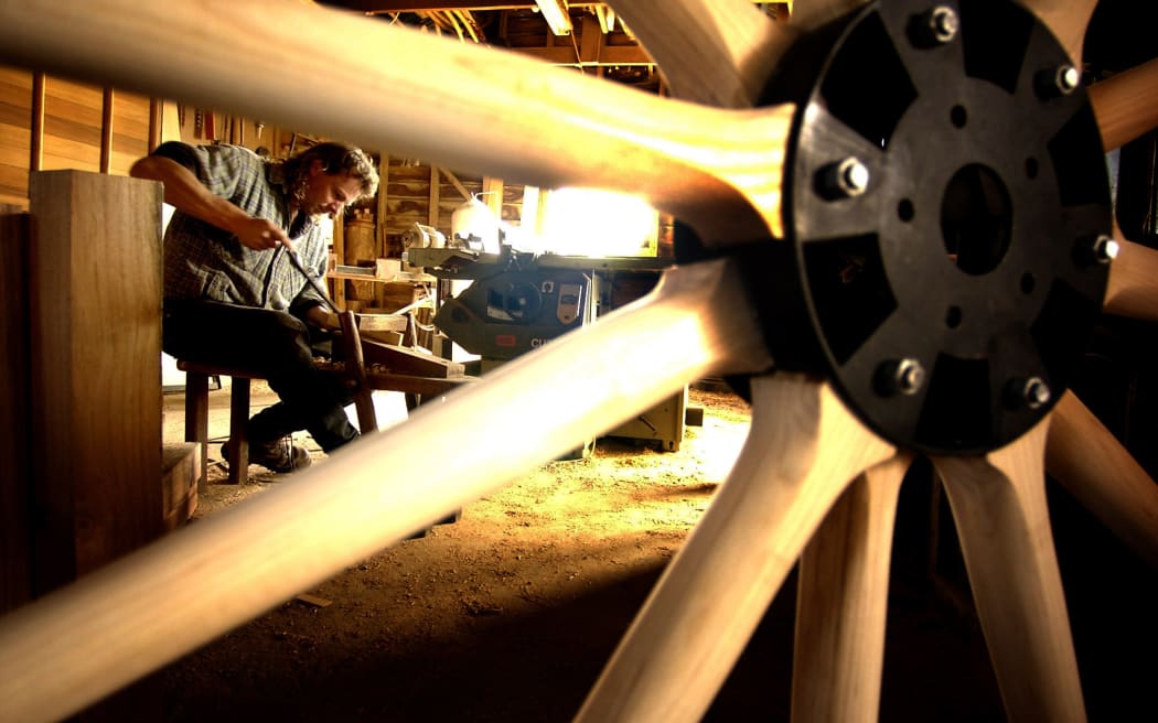 Man in workshop woodworking in a photo shot through the spokes of a wooden wheel