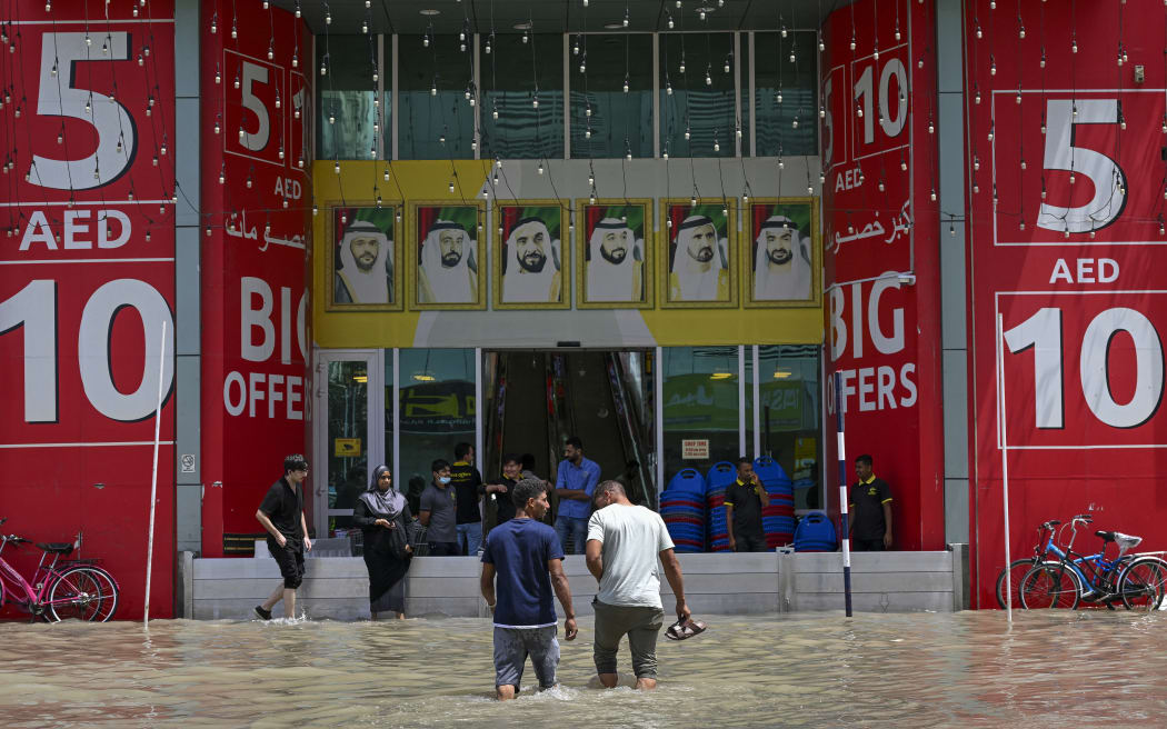 Men cross a flooded street following heavy rains in Sharjah on 17 April, 2024.