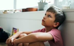 A boy day dreaming alone in a room.