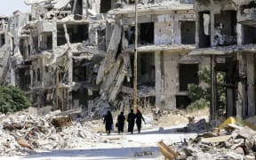 This file photo taken on September 19, 2016 shows Syrian women walking in between destroyed buildings in the government-held Jouret al-Shiah neighbourhood of the central Syrian city of Homs.