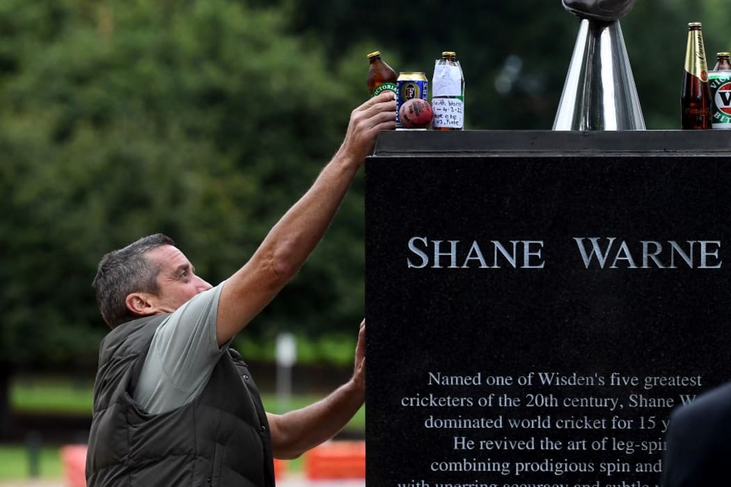 A man places a can of beer at the base of a statue of former Australian cricketing great Shane Warne at the Melbourne Cricket Ground, in Melbourne on March 5, 2022.