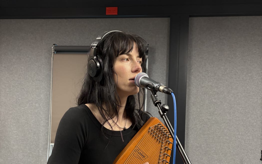 Georgia Knight is singing into a microphone and playing the autoharp. The mic cable is blue.
