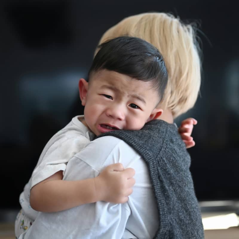 An infant boy cries and is held by his mother.