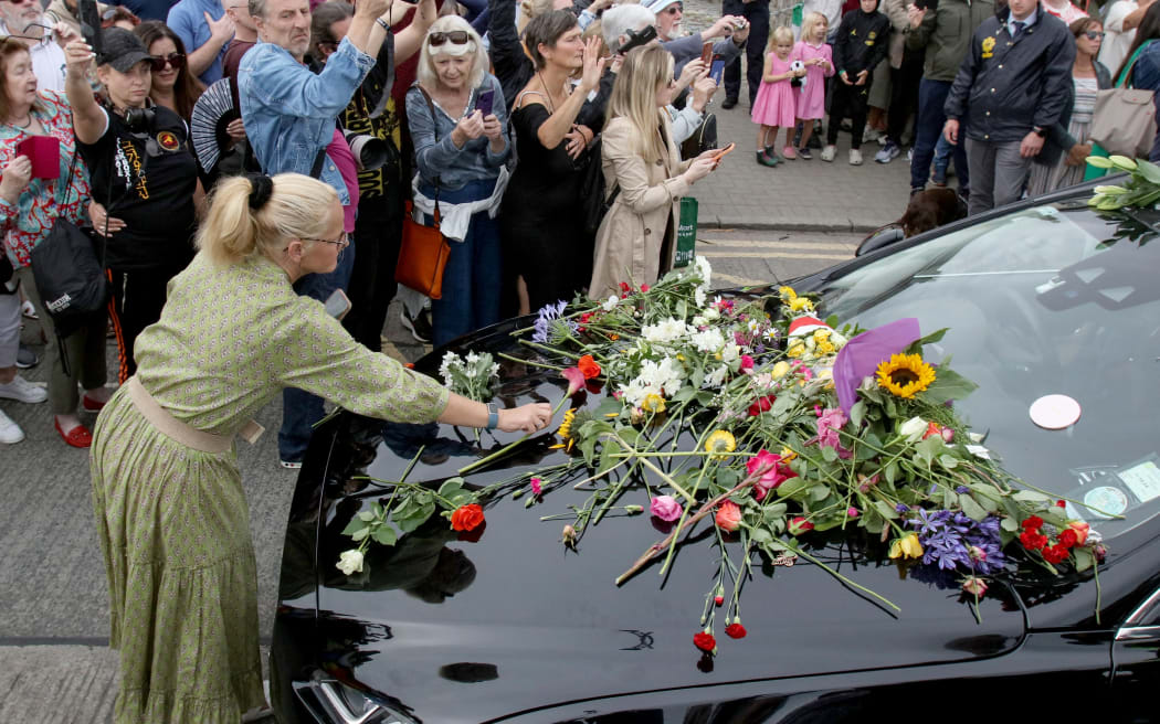 People lay flowers and tributes on the hearse during the funeral procession of late Irish singer Sinead O'Connor, outside the former home in Bray, eastern Ireland, ahead of her funeral on August 8, 2023. A funeral service for Sinead O'Connor, the outspoken singer who rose to international fame in the 1990s, is to be held on Tuesday in the Irish seaside town of Bray. (Photo by PAUL FAITH / AFP)