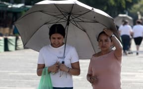 People protect themselves from the sun during a heat wave hitting the country, in Guadalajara, Jalisco state, Mexico, on May 9, 2024. More than a dozen states in Mexico reached a record maximum of 45°C. (Photo by ULISES RUIZ / AFP)