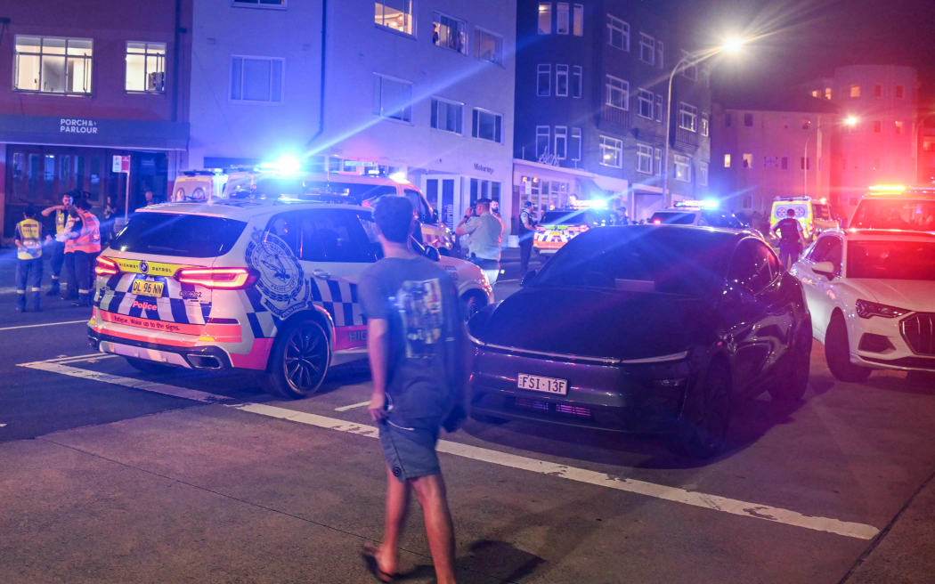 Police and health workers gather on a road after a shooting incident at Bondi Beach in Sydney on December 14, 2025. Australian police said two people were in custody following reports of multiple gunshots on December 14 at Sydney's famed Bondi Beach, urging the public to take shelter. (Photo by Saeed KHAN / AFP)