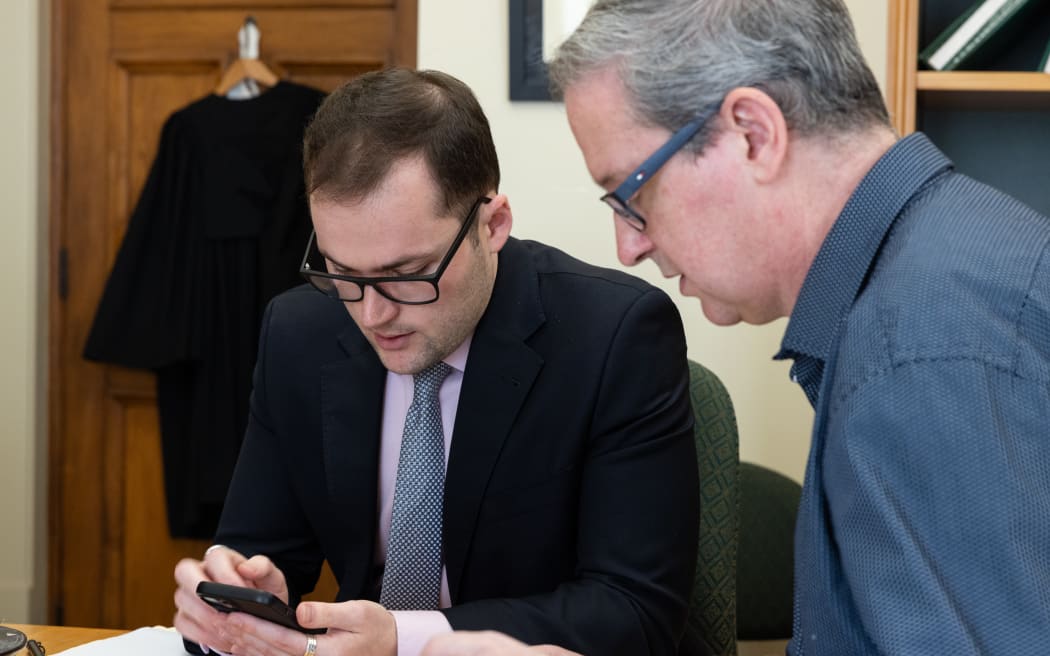 National's House Advisor Louis Donovan looks up some additional evidence on his phone in case it is necessary as David Bagnall assesses the authentication provided - it isn't needed.