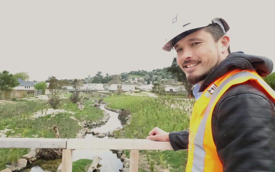 Man in hi vis vest stands on bridge looking at replanted stream