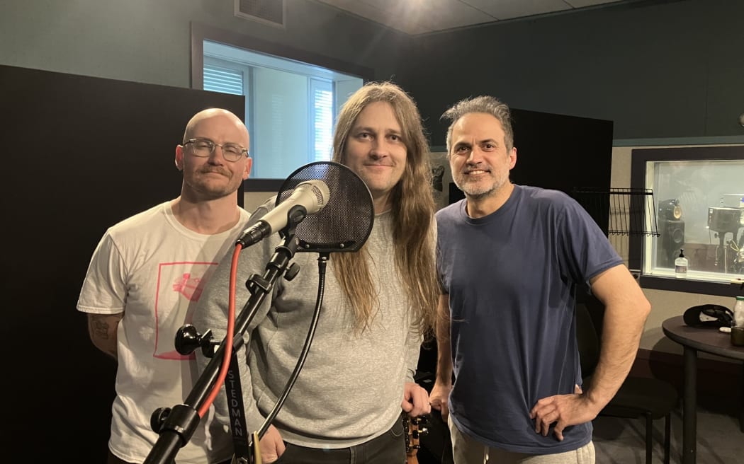 The band Tom Lark stand behind a microphone in the RNZ Wellington studio. They are a three piece band.
