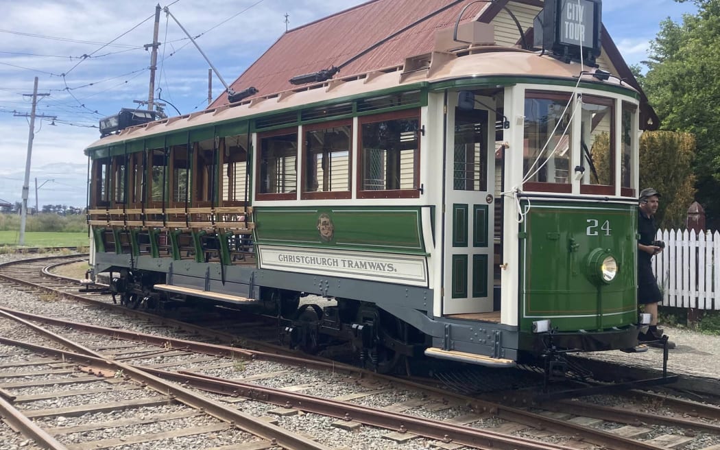 A restored tram sitting on railway tracks. It is white with green panels and red windows.