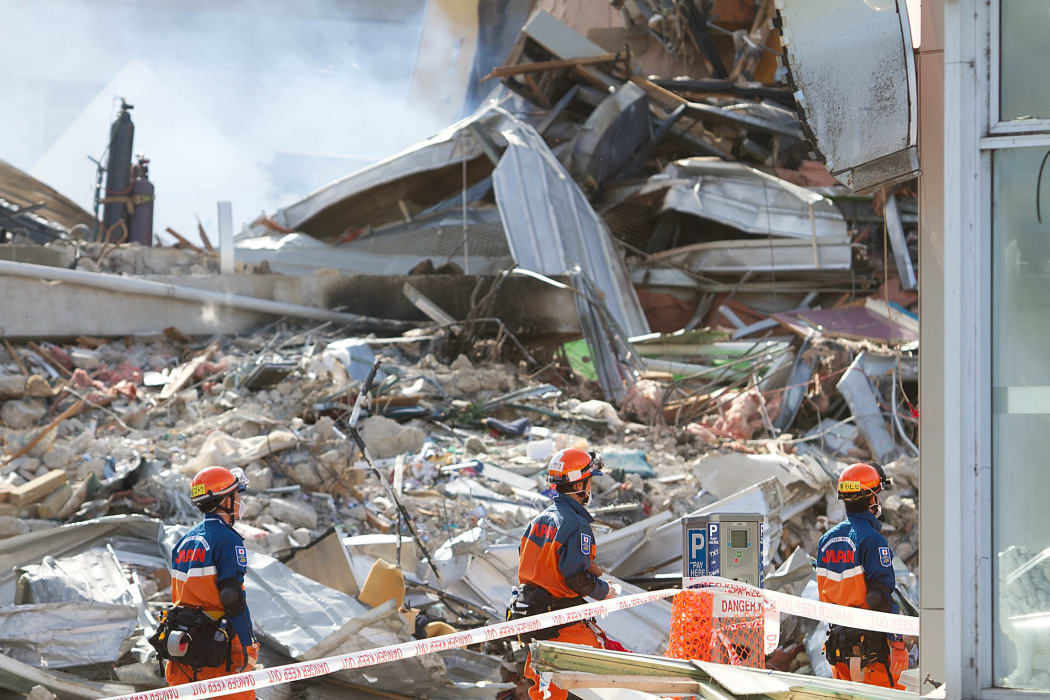 Japanese rescuers walk past the smoking ruins of the CTV building.