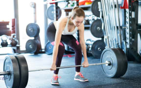 A young woman lifts a heavy looking barbell.