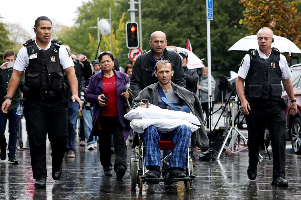 Temel Atacocugu (c), a survivor of the  mosque attacks, leaves the Christchurch District Court after the alleged gunman's second court appearance.