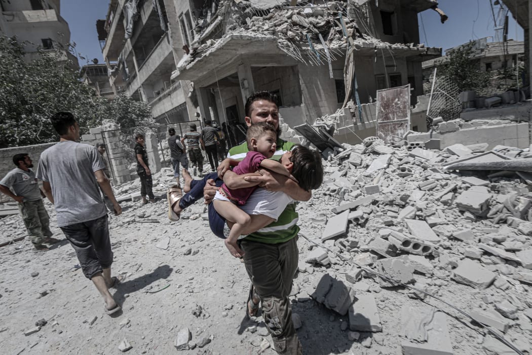 A Syrian man carries kids as search and rescue works are being carried out at the site after airstrikes of Russia and Assad Regime over Arihah district of Idlib, Syria on July 24, 2019.