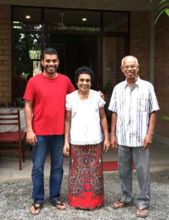 Sanjana Hattotuwa - a smiling man in a red tshirt - stands next to his elderly parents who are also smiling.