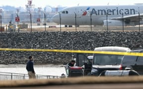 An American Airlines plane prepares to take off as investigators carry pieces of wreckage from the waters of the Potomac River after American Airlines flight 5342 on approach to Reagan National Airport crashed into the river after colliding with a US Army helicopter, near Washington, DC, on January 30, 2025. There are likely no survivors from a collision between a passenger jet and US Army helicopter in Washington, officials said Thursday, as recovery operations pulled 28 bodies from the river into which both crashed.