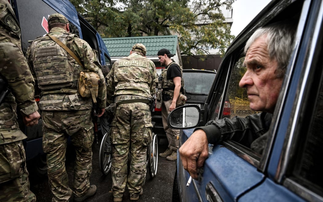 Police officers of the ''White Angel'' special unit hand over a mobility-impaired evacuated man to volunteers in the village of Pokrovske, Synelnykove district, which serves as an intermediate hub where people evacuated from frontline villages are brought before volunteers from various charitable organizations transport them further to transit centers, in Dnipropetrovsk region, Ukraine, on October 9, 2025 (Photo by Dmytro Smolienko/Ukrinform/NurPhoto). NO USE RUSSIA. NO USE BELARUS. (Photo by Ukrinform/NurPhoto) (Photo by Dmytro Smolienko / NurPhoto via AFP)
