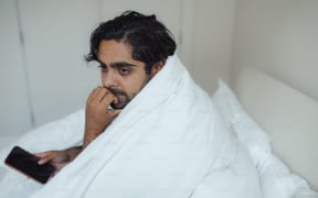 A man in bed with mobile phone and worried look
