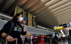 A passenger wearing a respiratory mask speaks on her smartphone by the departures board at Rome's Fiumicino airport.