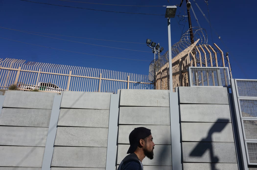 A pedestrian walks towards the port of Entry at the US-Mexico border wall.