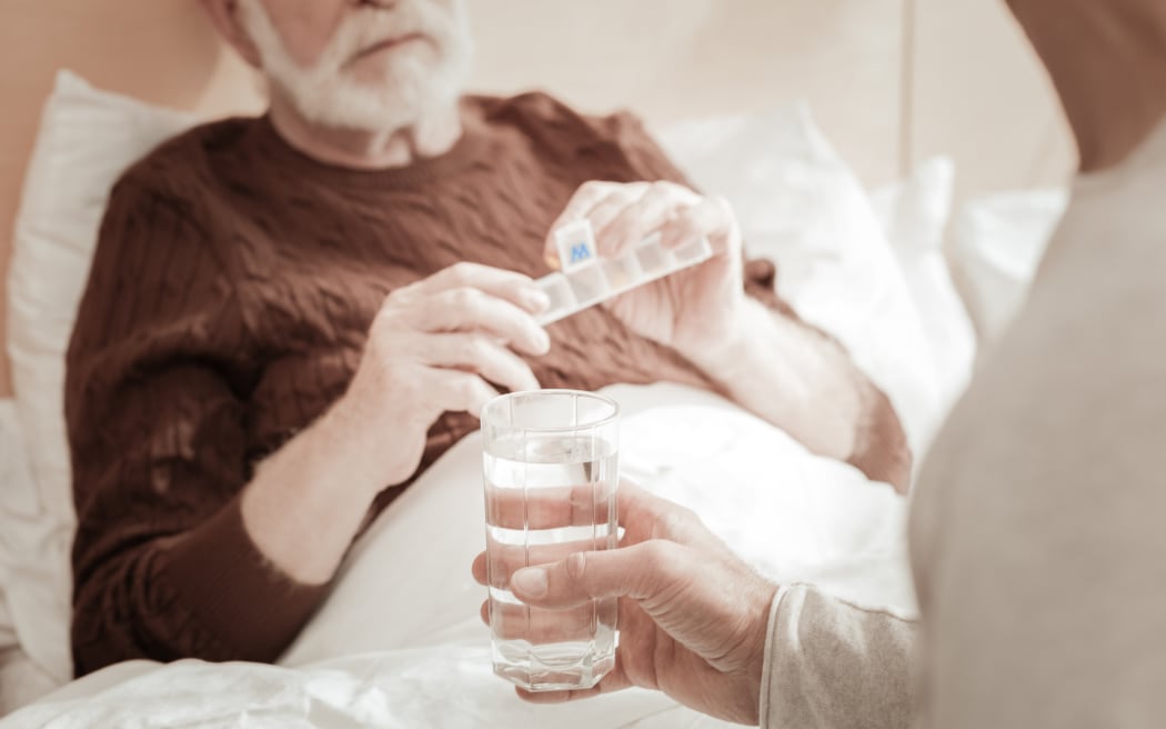 Mężczyzna w łóżku, który ma zamiar zażyć leki.