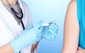 16341754 - doctor holding syringe with vaccine into patient's shoulder on blue background