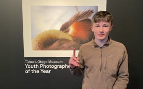 Monty McGee standing by his photo of a native crested grebe. The photo is called Pūteketeke Yoga.