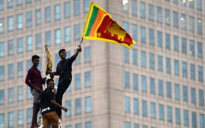 A man waves Sri Lanka's national flag after climbing a tower near presidential secretariat in Colombo on 1 July, 2022, after it was overrun by anti-government protesters.