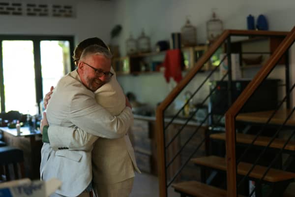 An older man hugging a young man while smiling at a home.