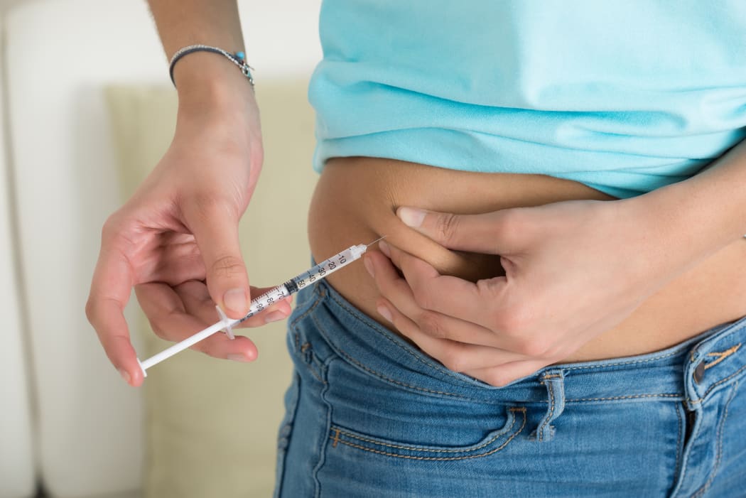 Midsection of diabetic young woman injecting stomach at home