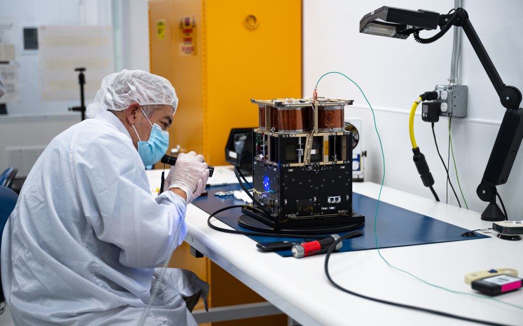 Mariano Perez, quality assurance engineer at NASA Ames, inspects the Advanced Composite Solar Sail System spacecraft. When the composite booms and solar sail deploy in orbit, they will measure about 860 square feet (80 square meters) – about the size of six parking spots. Credit: NASA/Brandon Torres