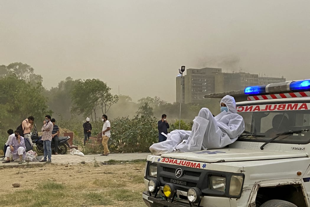 A driver wearing protective gear sits on the bonnet of an ambulance while waiting for the dead body of a Covid-19 coronavirus victim to be taken for burial at a graveyard in New Delhi on April 16, 2021.
