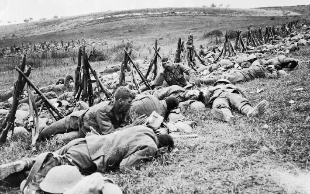 Men of the Royal Warwickshire Regiment, their rifles stacked nearby, lying exhausted in the grass in a rear area.