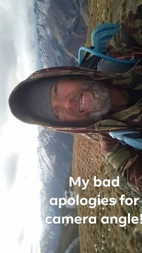Too cold to use his hands properly, Bruce tries to take a photo somewhere near Wanaka. The image is of him in the foreground with a snow range behind him but is is portrait form when it should be in landscape. the caption reads "my bad apologies for camera angle!"