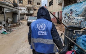 A man collects trash while wearing a jacket bearing the logo of the United Nations Relief and Works Agency for Palestine Refugees in the Near East (UNRWA), along a street in the city of Jenin in the occupied West Bank on January 30, 2024. At least 12 countries -- with top donors the United States and Germany joined by New Zealand on January 30 -- have suspended their funding to UNRWA over Israeli claims that some of its staff members were involved in the October 7 attack. (Photo by Jaafar ASHTIYEH / AFP)