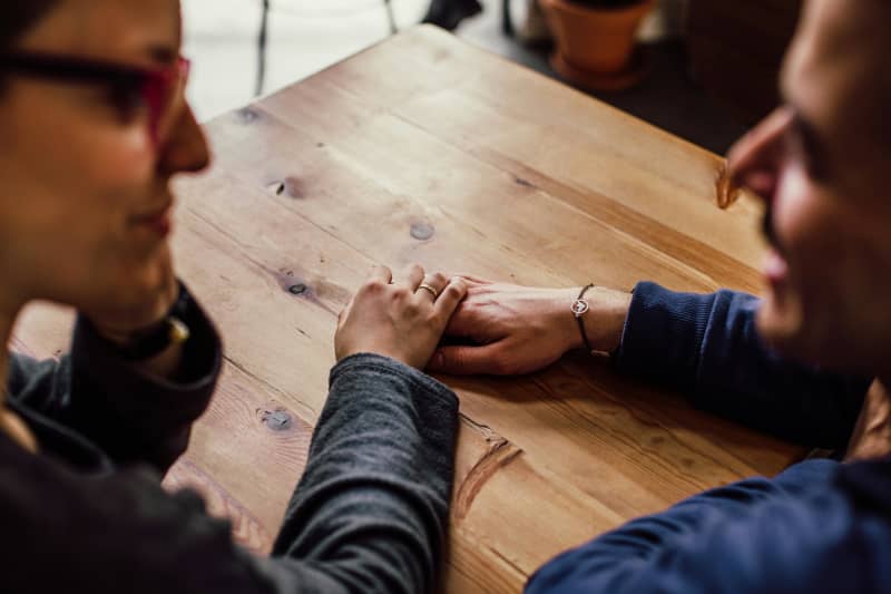 A couple looks at each other and hold hands over a wooden table
