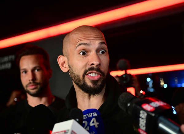 Andrew Tate (R) and his brother Tristan (L) speak to the media as they arrive in Romania back from US, in Bucharest March 22, 2025. Self-described misogynist influencer Andrew Tate return to Romania, where he is facing rape and human trafficking charges, after a trip to the US. The British-American figurehead of the online masculinist movement travelled to Florida, together with his brother, last month, marking the first time he had been out of the eastern European country since his 2022 arrest. Under judicial supervision, the Tates need to report to authorities on March 24, a no-show potentially leading to "preventive arrest", according to Romanian authorities. (Photo by Daniel MIHAILESCU / AFP)