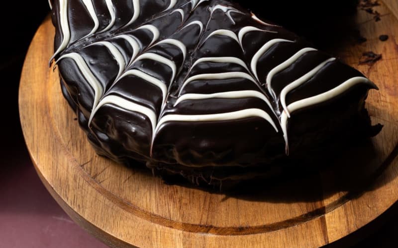 A dark chocolate cake with thick icing sits on a round wooden board.