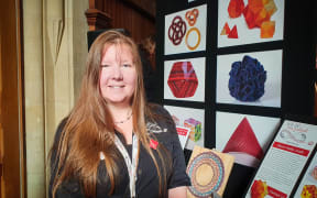 Jeannette McLeod, Maths Craft director stands in front of a poster with pictures of crafts on it.