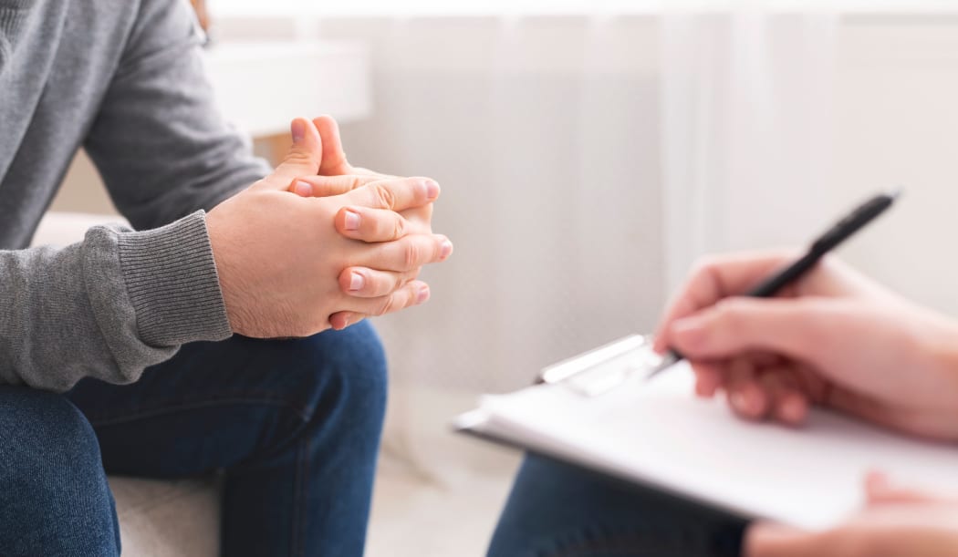 Therapist writing notes during counseling session with single man sitting on couch, panorama, empty space