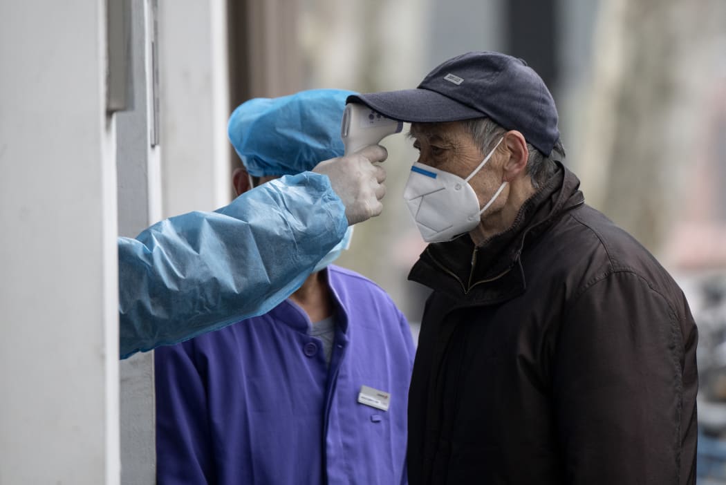 An elderly man wearing a face mask has his temperature checked before entering a community hospital in Shanghai on 13 February 2020.