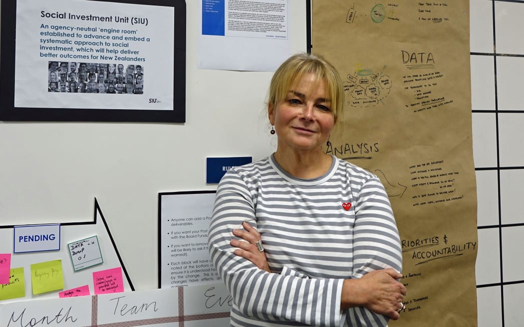 Woman in striped top stands in front of wall will long banner of paper  with work thoughts wirtten on it