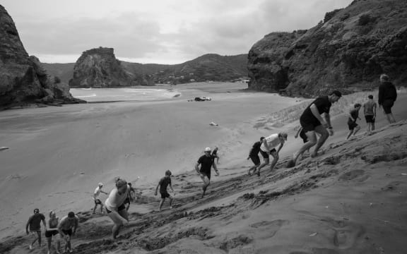 People struggling to run up a sand dune.