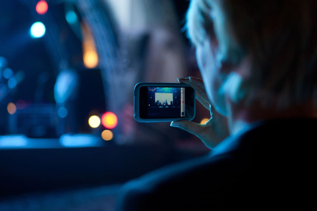 Woman use mobile phone shooting video photo of concert in front of stage at night with beautiful blurred bokeh from the lights in background