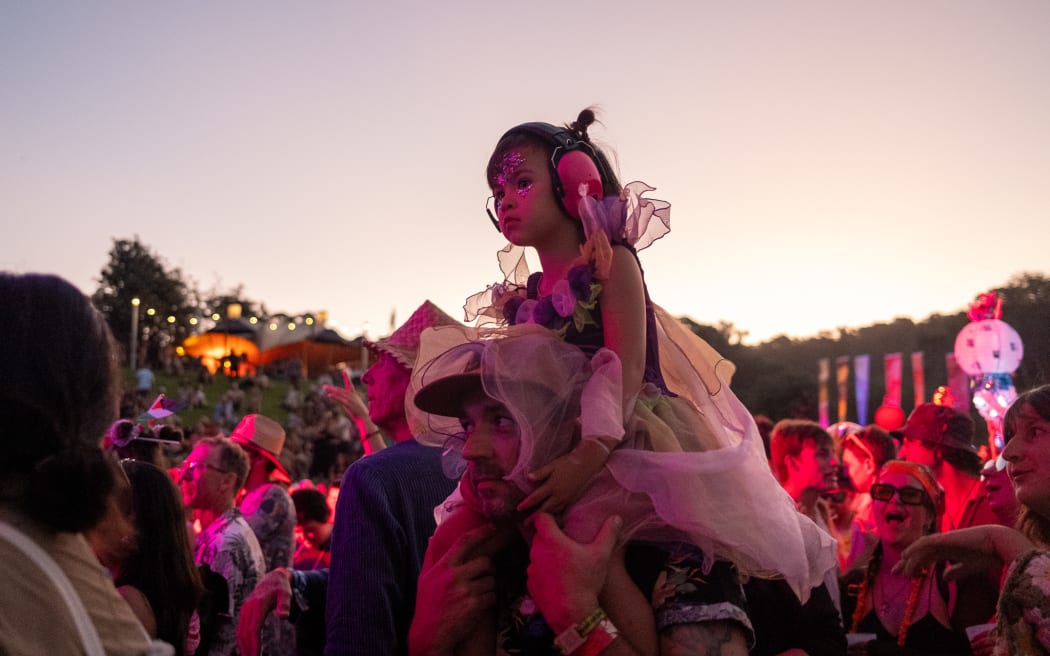 A young child wearing earmuffs gets a shoulder ride at Splore