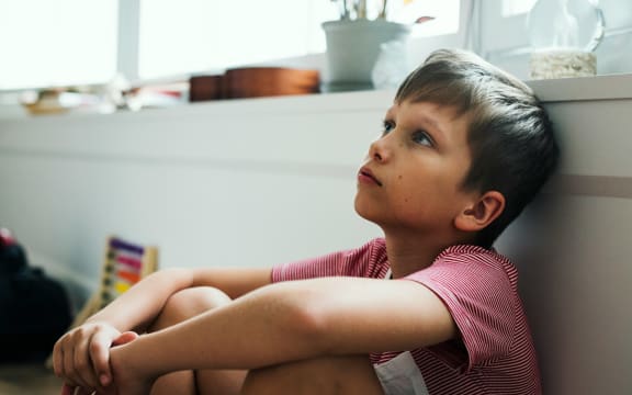 A boy day dreaming alone in a room.