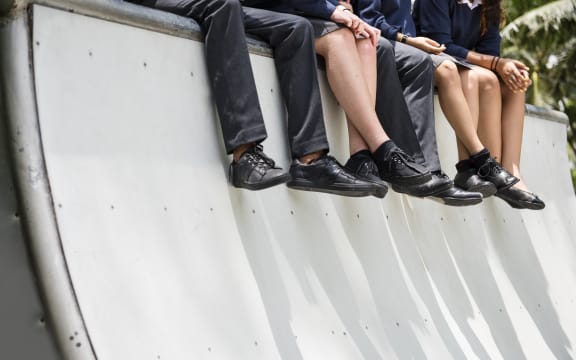 A group of school children in uniform sit on the edge of a skateboard bowl