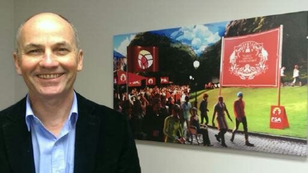 Glenn stands in front of  an art work of a PSA protest