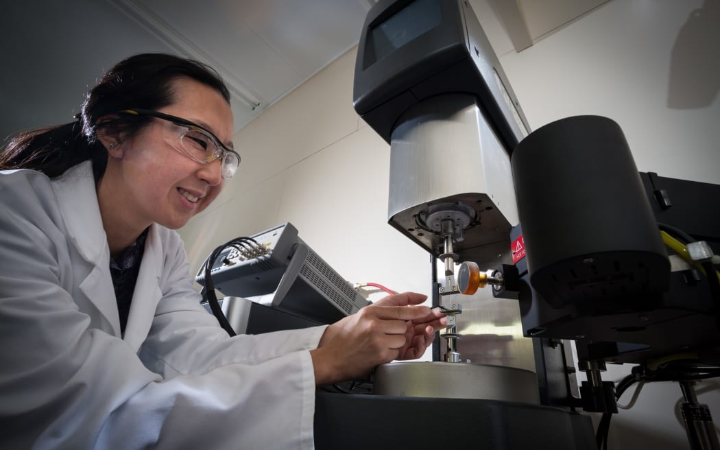 Marie-Joo is wearing a lab coat and safety glasses as she works with a piece of lab machinery.
